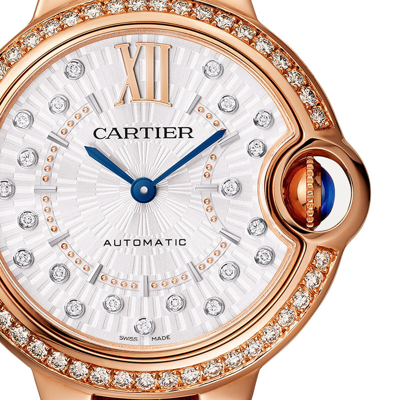 Close-up of the Ballon Bleu de Cartier watch in rose gold by Cartier, showcasing a diamond-studded bezel, Roman numeral XII, blue hands, and AUTOMATIC on its silver dial.
