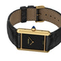 The Cartier Tank Louis Cartier watch features a gold case, black square face, black leather strap, and a blue gemstone crown.