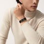 A person in a cream turtleneck displays a Cartier Tank Louis Cartier gold watch with a black strap on their wrist.