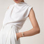 A woman in a sleeveless white blouse and high-waisted white pants has one hand in her pocket, accessorized with the elegant La Panthère de Cartier watch by Cartier.