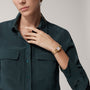 A woman in a dark green button-up shirt showcases a Cartier Panthère de Cartier Small Model gold wristwatch on her left wrist, her hand poised near her collar.