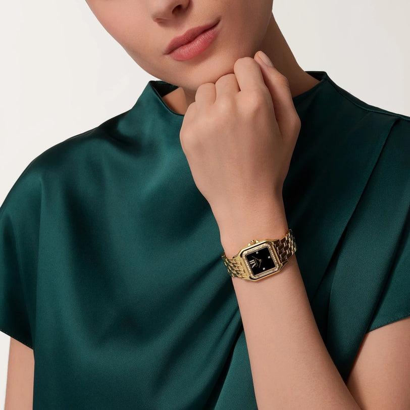Wearing a dark green satin top, a person showcases the Cartier Panthère de Cartier watch with a black rectangular face on their left wrist, epitomizing timeless chic.