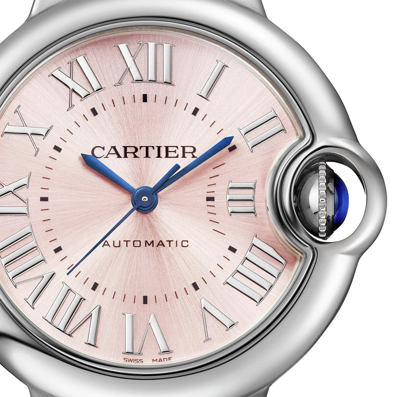 Close-up of a Cartier Ballon Bleu de Cartier watch face featuring Roman numeral markers, blue hands, a pink sunray dial, and a crown adorned with a blue cabochon.