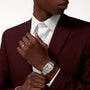 Wearing a burgundy suit and white shirt, a person adjusts the Cartier Tank Française watch on their wrist, a gold ring visible on their left hand—a true design icon.