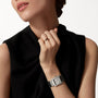 A person in a sleeveless black top and simple ring showcases the Cartier Tank Française watch on their wrist, holding their hand near their face against a plain background.