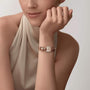 A woman in a sleeveless beige top showcases a Cartier La Panthère de Cartier watch with a decorative band on her left wrist, her chin resting on her hand.