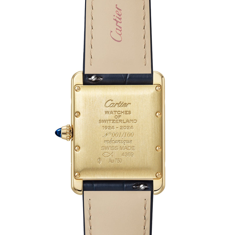 Close-up of the back of a Cartier Tank Américaine wristwatch with a gold Art Deco case featuring engraved markings and a blue gemstone on the crown, paired with beige leather straps.