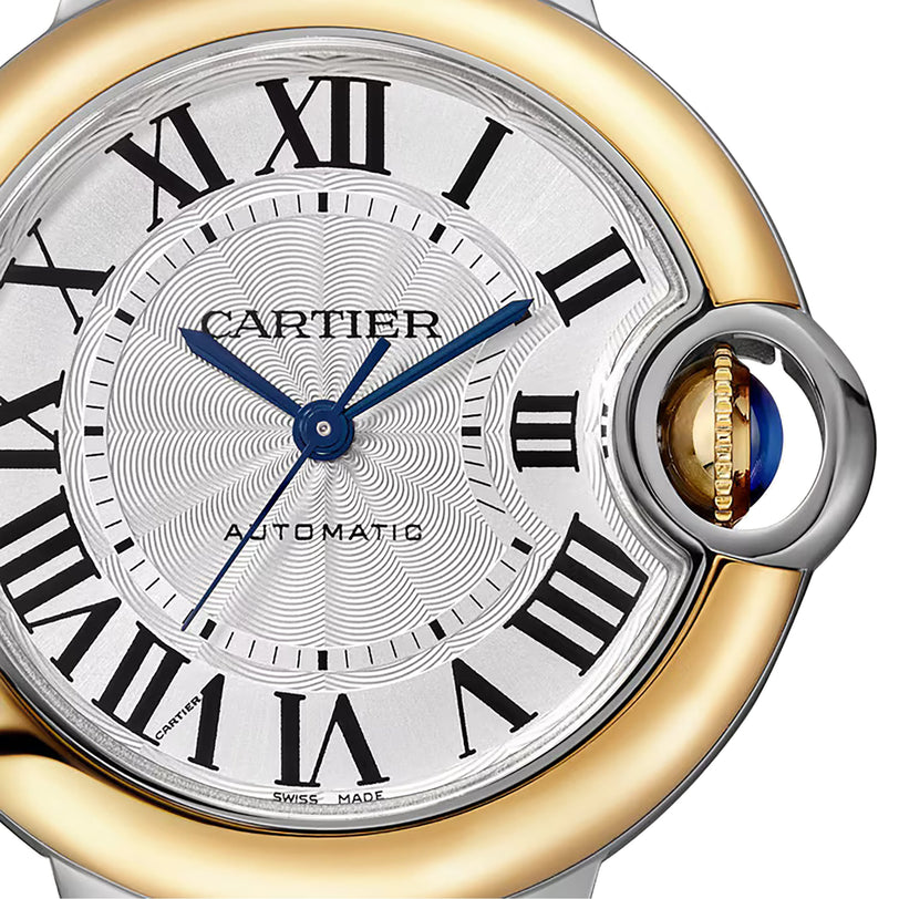 Close-up of a Cartier Ballon Bleu de Cartier watch face with Roman numerals, blue hands, and an 18K yellow gold and silver bezel. The crown is accented with a vivid blue sapphire cabochon.