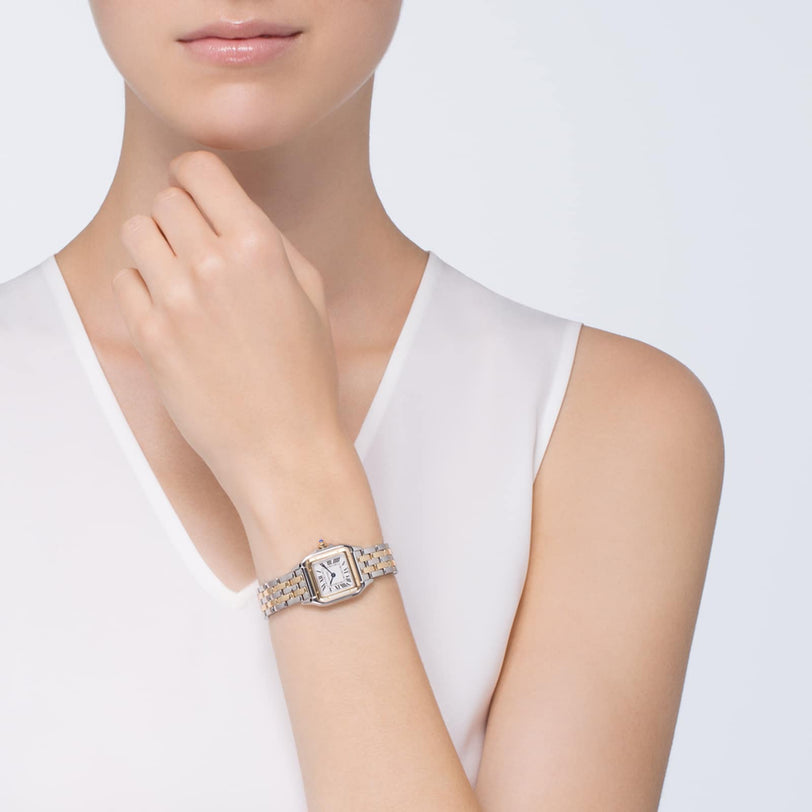 A woman in a sleeveless white top showcases a Cartier Panthère de Cartier Small Model watch with a rectangular face and metal link band, crafted in 18K yellow gold, on her left wrist.