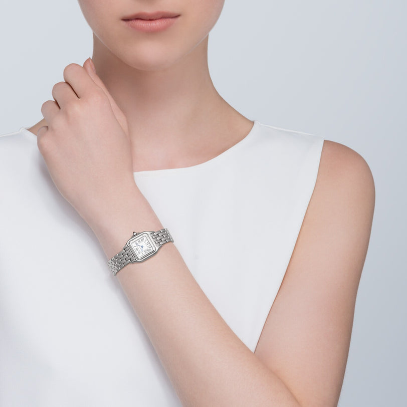 A person in a sleeveless white top wears the Cartier Panthère de Cartier Small Model watch, featuring a rectangular face and metallic band on their left wrist, exuding timeless elegance.
