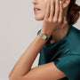 A woman in a green satin top wears the Panthère de Cartier Small Model wristwatch by Cartier in rose gold and diamonds, touching her face with her left hand against a neutral background.