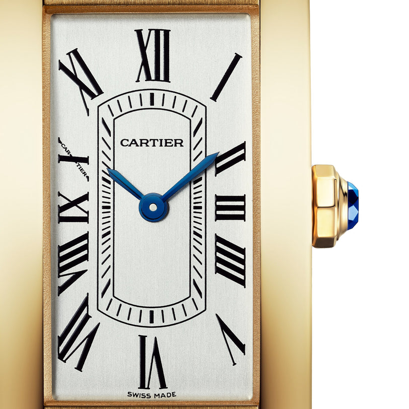 Close-up of a Cartier Tank Américaine watch face, an elegant timepiece featuring blue hands, Roman numerals, gold casing, and a crown adorned with a blue gemstone.
