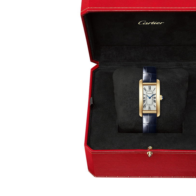 The Cartier Tank Américaine, a gold rectangular wristwatch with a black strap, is showcased in a signature red Cartier box lined with black fabric.