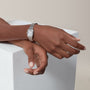 A person rests their hands on a white textured block, wearing the Panthère de Cartier Small Model by Cartier—a jewellery watch with a rectangular face, metal band, and elegant brilliant cut diamonds.