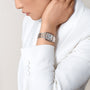 Person in a white blazer touches their neck, wearing the Panthère de Cartier watch by Cartier, featuring a diamond-set bezel and rectangular face with Roman numerals.