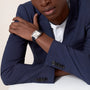A person in a navy blue suit with a white shirt sits with arms crossed, wearing a rectangular-faced Cartier Santos-Dumont watch.