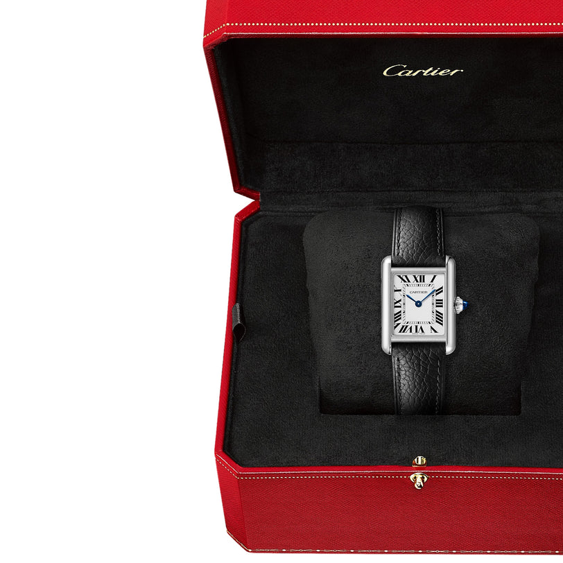 A Cartier Tank Must Solarbeat™ wristwatch with a rectangular face, silvered dial, and black leather strap is displayed in an open red Cartier box lined with black fabric.
