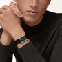 A person wearing a black long-sleeve top showcases the Cartier Tank Must de Cartier watch, featuring a rectangular face and black alligator-skin strap, on their wrist.