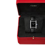 The Cartier Tank Must de Cartier watch, featuring a black rectangular face and black alligator-skin strap, is presented in a red Cartier box and operates with precise quartz movement.