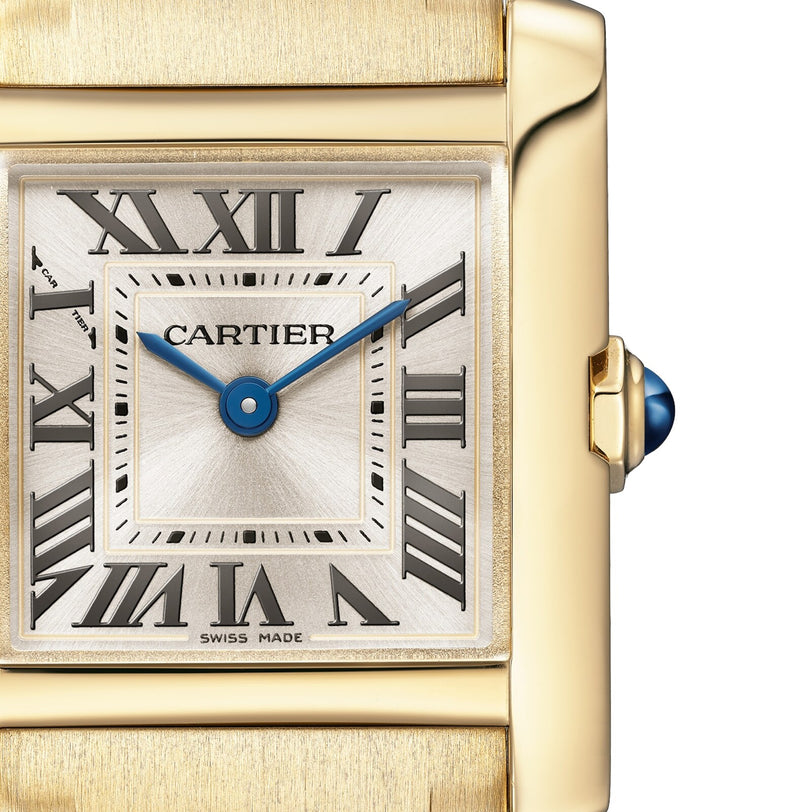 Close-up of the Cartier Tank Française watch, featuring a gold case, Roman numeral markers, blue hands, and a blue cabochon crown.