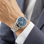 A person wearing an OMEGA Seamaster Aqua Terra 150M with a blue dial, paired with a grey suit jacket and white shirt.