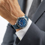 A person in a gray suit wears the OMEGA Seamaster Diver 300M with a textured blue dial, blue rubber strap, and OMEGA Calibre 8800 movement.