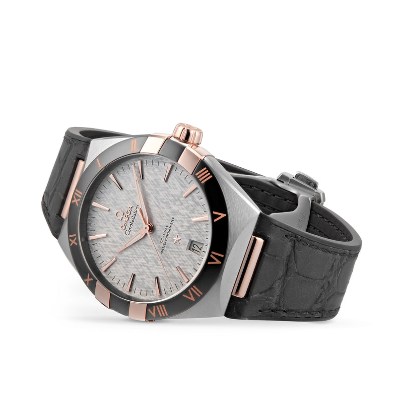 An OMEGA Constellation wristwatch with a textured silver dial, rose gold accents, black Roman numeral bezel, and black leather strap featuring the precise 8900 calibre movement. Displayed angled on a white background.