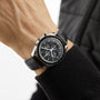 A person wearing an OMEGA Speedmaster Moonwatch Professional with a black leather strap, black dial, and the 3861 calibre movement.