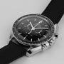 A close-up of the OMEGA Speedmaster Moonwatch Professional with a black dial, three subdials, black fabric strap, and precise 3861 calibre movement, photographed on a light background.