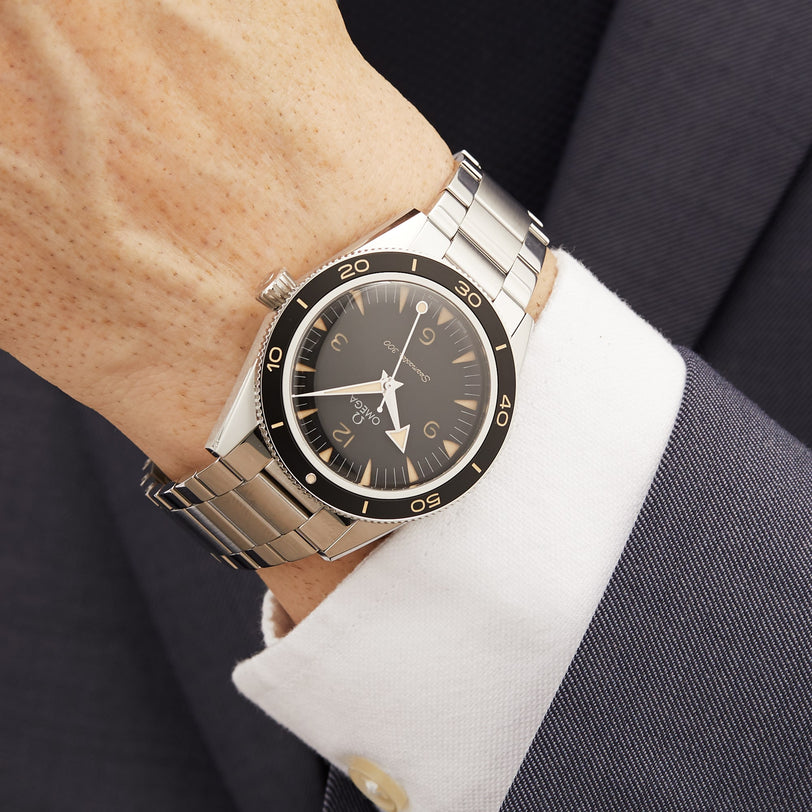A close-up of a wrist wearing the OMEGA Seamaster 300, featuring a black bezel and dial, powered by the Co-Axial Master Chronometer Calibre 8912, paired with a white shirt and dark suit jacket.