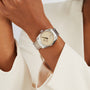 A person wearing an OMEGA Seamaster Aqua Terra 150M wristwatch with a beige dial and metallic band, dressed in an off-white blazer.