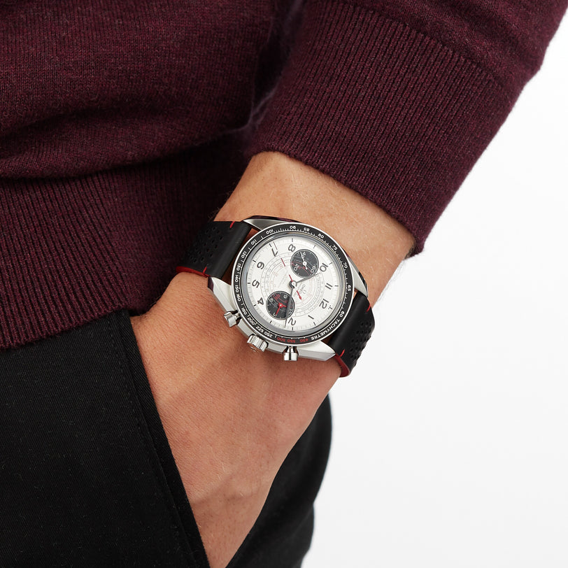 A person in a maroon sweater and black pants, hand in pocket, showcases the OMEGA Speedmaster Chronoscope with a 43mm stainless steel case and black strap.