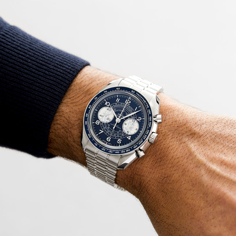 An OMEGA Speedmaster Chronoscope with a blue dial and silver strap is worn on a persons left wrist.