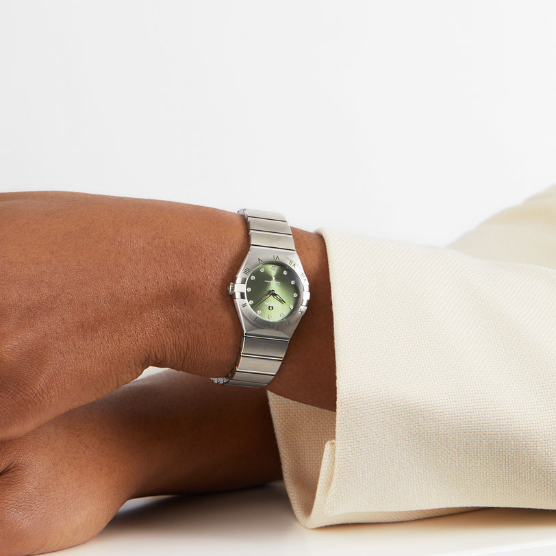 A person wearing the OMEGA Constellation with a matcha green dial and stainless steel case rests their arm on a white surface, their light-colored jacket accentuating the watch’s elegant style.