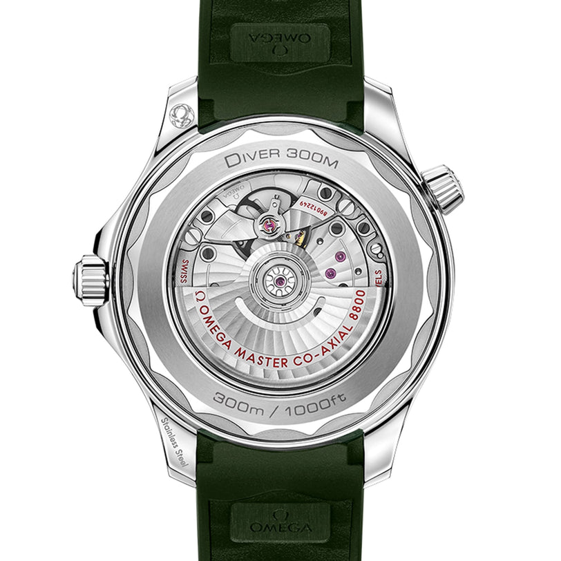 The image shows the transparent case back of an OMEGA Seamaster Diver 300M, displaying its mechanical movement and engravings, with a green strap attached.