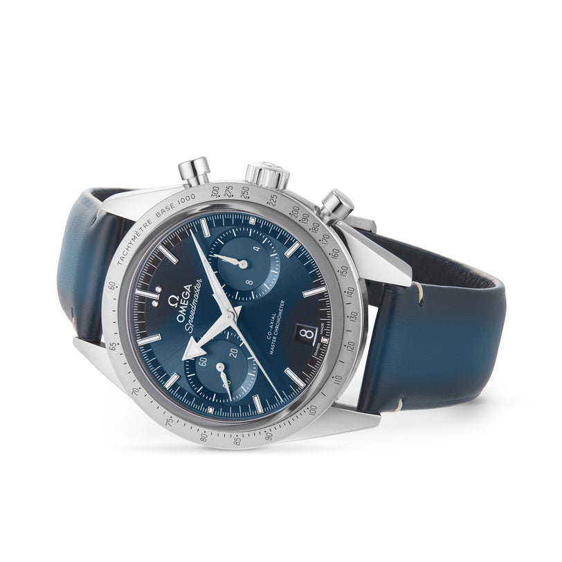 An OMEGA Speedmaster 57 chronograph with a blue dial, blue leather strap, silver bezel, tachymeter scale, and three subdials is shown against a white background.