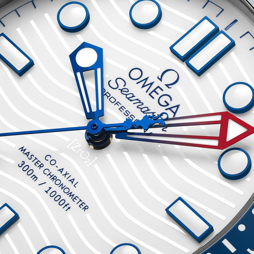 Close-up of the OMEGA Seamaster Diver Americas Cup 300M watch face, featuring blue and red hands, wave pattern background, regatta scale, and brand details. Powered by the Co-Axial Master Chronometer Calibre 8806 movement.