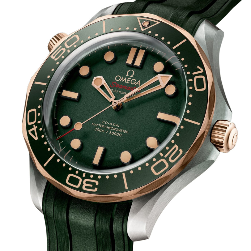 The OMEGA Seamaster Diver 300M features a green dial, 9K Bronze Gold bezel, gold crown, green rubber strap, and is powered by the Co-Axial Master Chronometer movement. Time shown is 10:10.