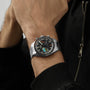 A person wearing an OMEGA Speedmaster Pilot, featuring a black dial and colorful details, dressed in a black jacket.