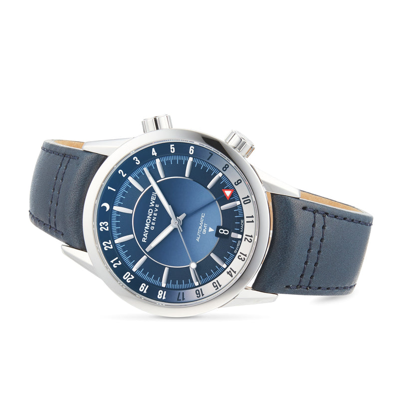 The Raymond Weil Freelancer GMT Blue Dial wristwatch features a blue dial, dual crowns, date display, and blue leather strap—embodying Swiss quality—shown at an angle against a white background.