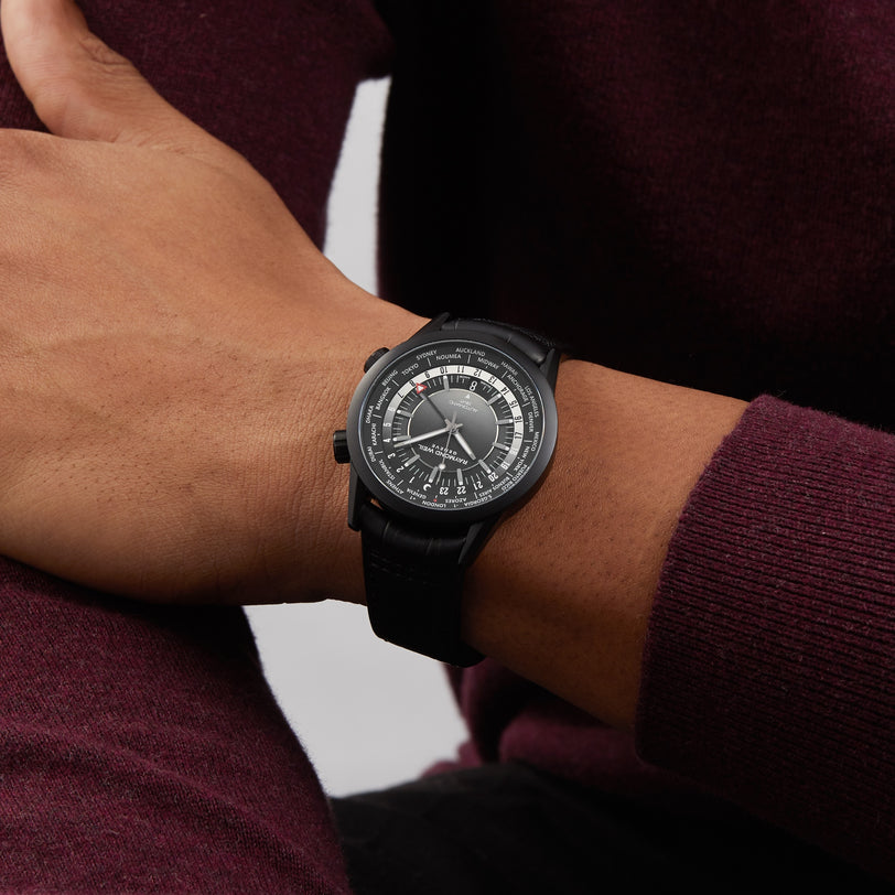 A person wearing a Raymond Weil Freelancer GMT Worldtimer with a black dial, stainless steel case, and black strap, dressed in a burgundy sweater.