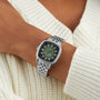 A person wearing a Raymond Weil Freelancer Automatic 60 Diamonds Green Dial wristwatch paired with a white knit sweater.