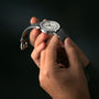 A person holds and inspects a Raymond Weil Millesime Automatic Small Seconds Silver Sector Dial watch with a grey leather strap, highlighting its refined craftsmanship against a dark background.