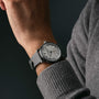 A person wearing a gray long-sleeve sweater and a Raymond Weil Millesime Automatic Small Seconds Silver Sector Dial watch with a light face and dark strap.