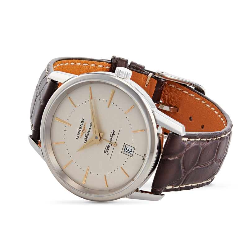 The Longines Flagship Heritage is a silver automatic wristwatch with a stainless steel case, white dial, gold hour markers, date display, and a brown leather strap.