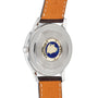 The Longines Flagship Heritage watch features a brown leather strap, stainless steel case, and a central medallion with a blue background and gold ship design on the back, housing an automatic movement.