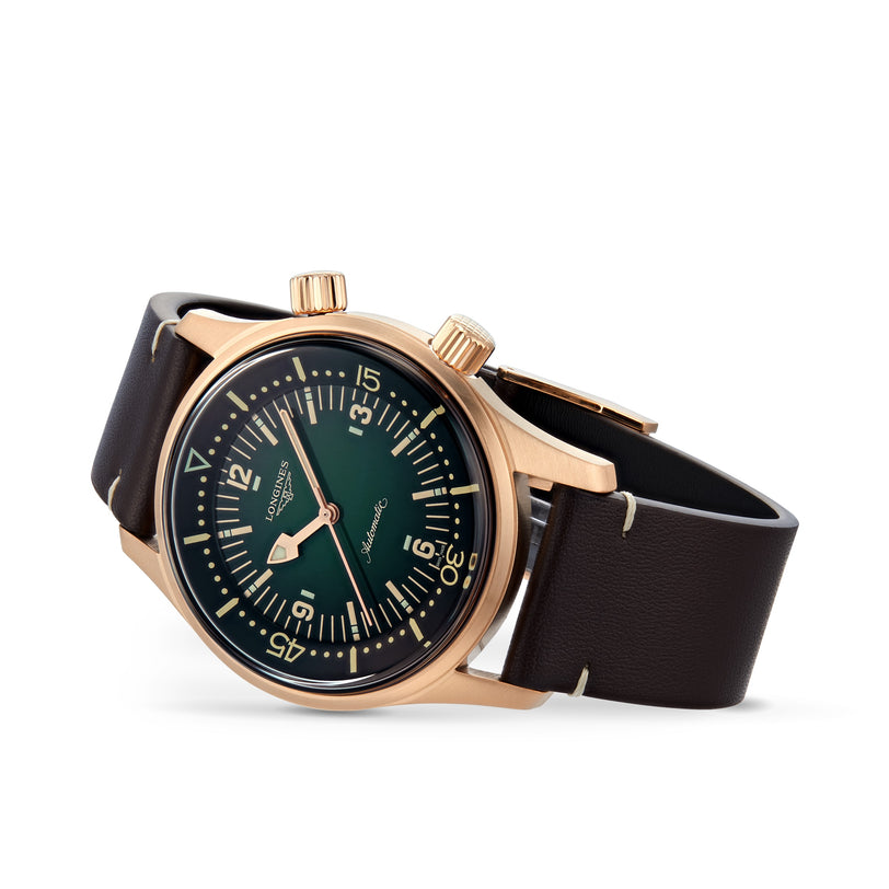 The Longines Legend Diver Bronze watch features a dark green dial, two crowns, white numerals, and a brown leather strap, displayed on a white background.