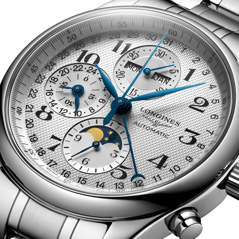 Close-up of the Longines Master Collection Chrono Moonphase watch in silver, featuring blue hands, automatic movement, moonphase, and subdials for time, date, day, month, and 24-hour on a textured white face.