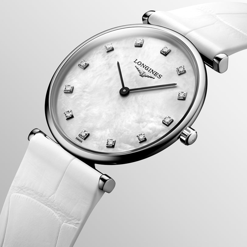 A close-up of the Longines La Grande Classique de LONGINES wristwatch featuring a white leather strap, white mother-of-pearl dial, and diamond hour markers on a light gray background.
