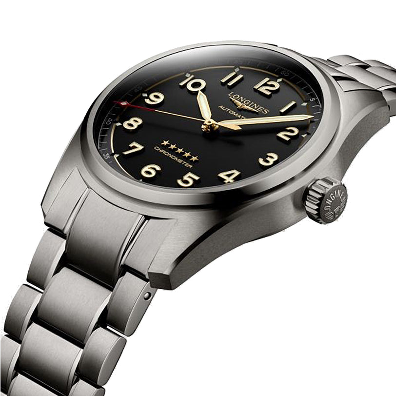 The Longines Spirit features a stainless steel case, black dial with gold numerals and hands, metal bracelet, and a prominent winding crown on the right.
